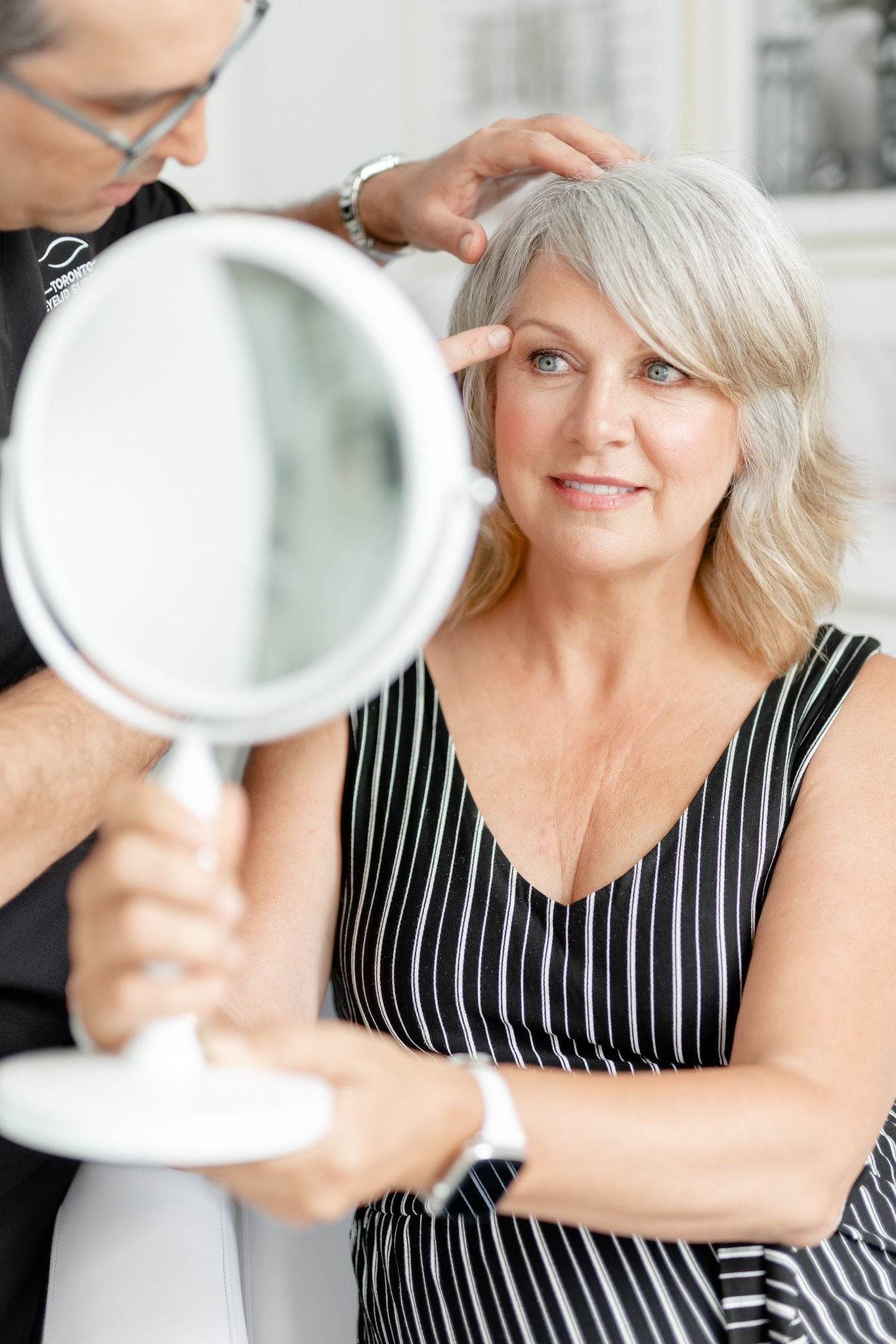 Female patient admiring results in handheld mirror after aesthetic consultation with Dr. Babak Maleki at his Toronto clinic