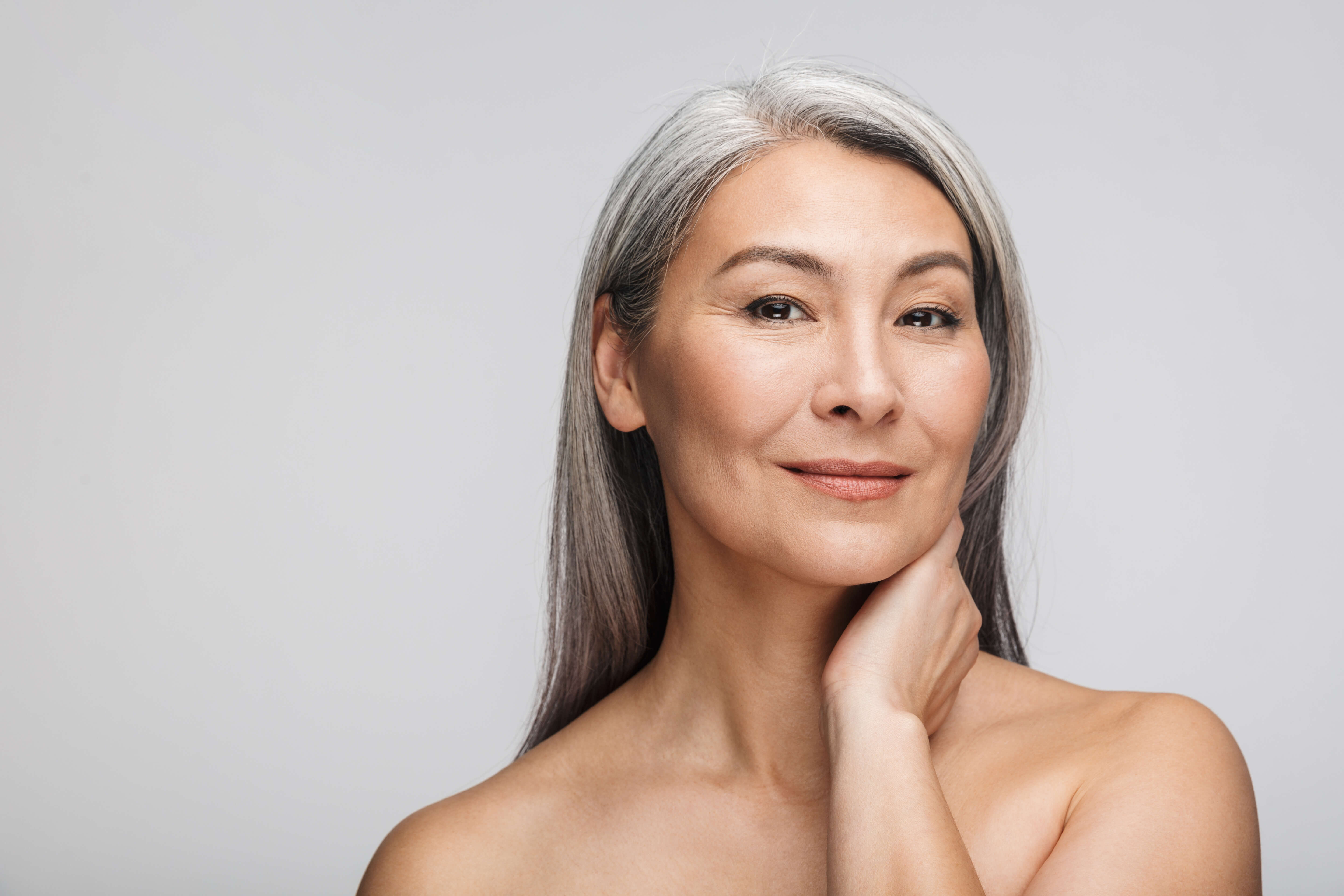 Woman with gray hair touching her neck against a light gray background
