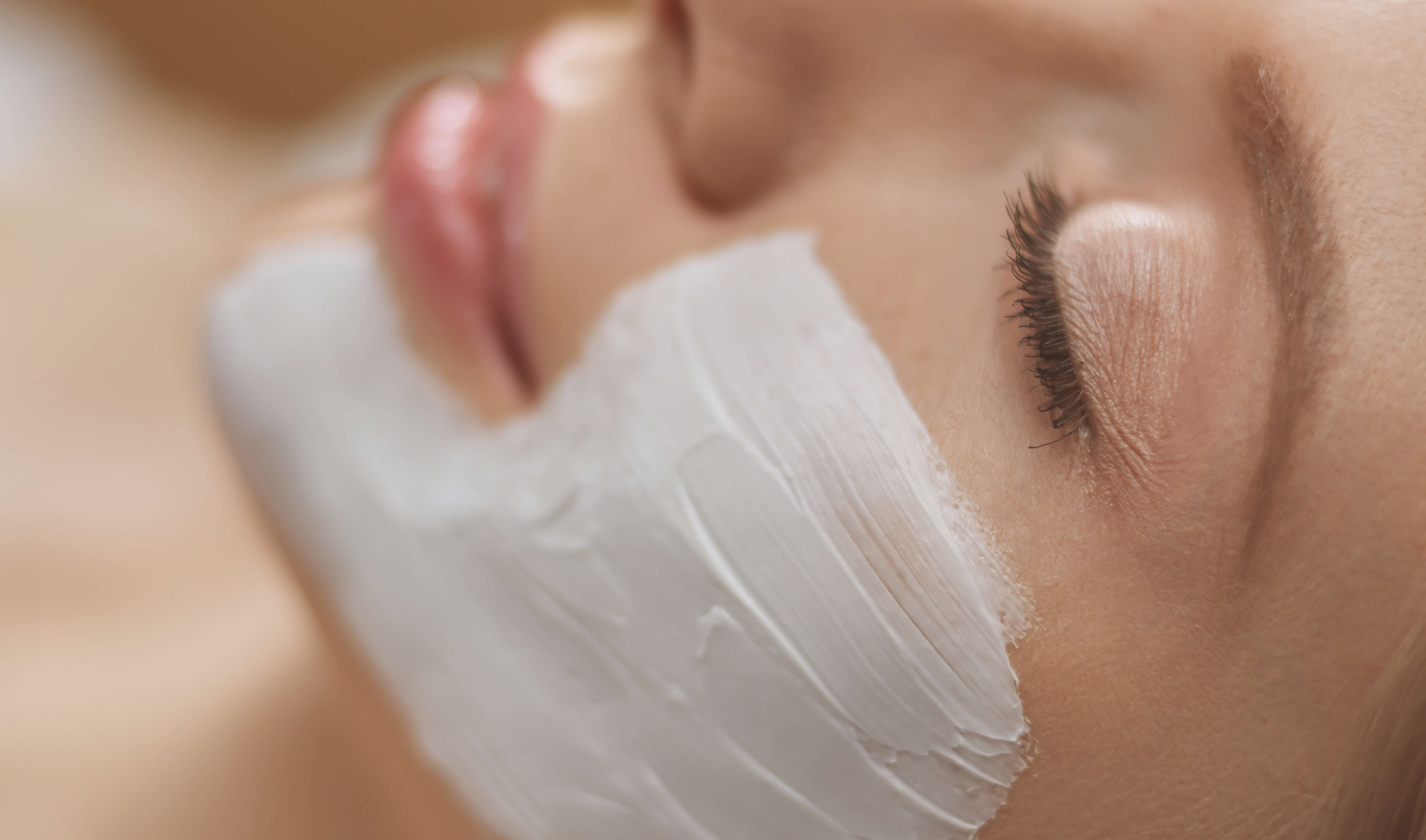 Woman receiving chemical peel treatment with a brush applying white exfoliating solution to the face for skin renewal and texture improvement.