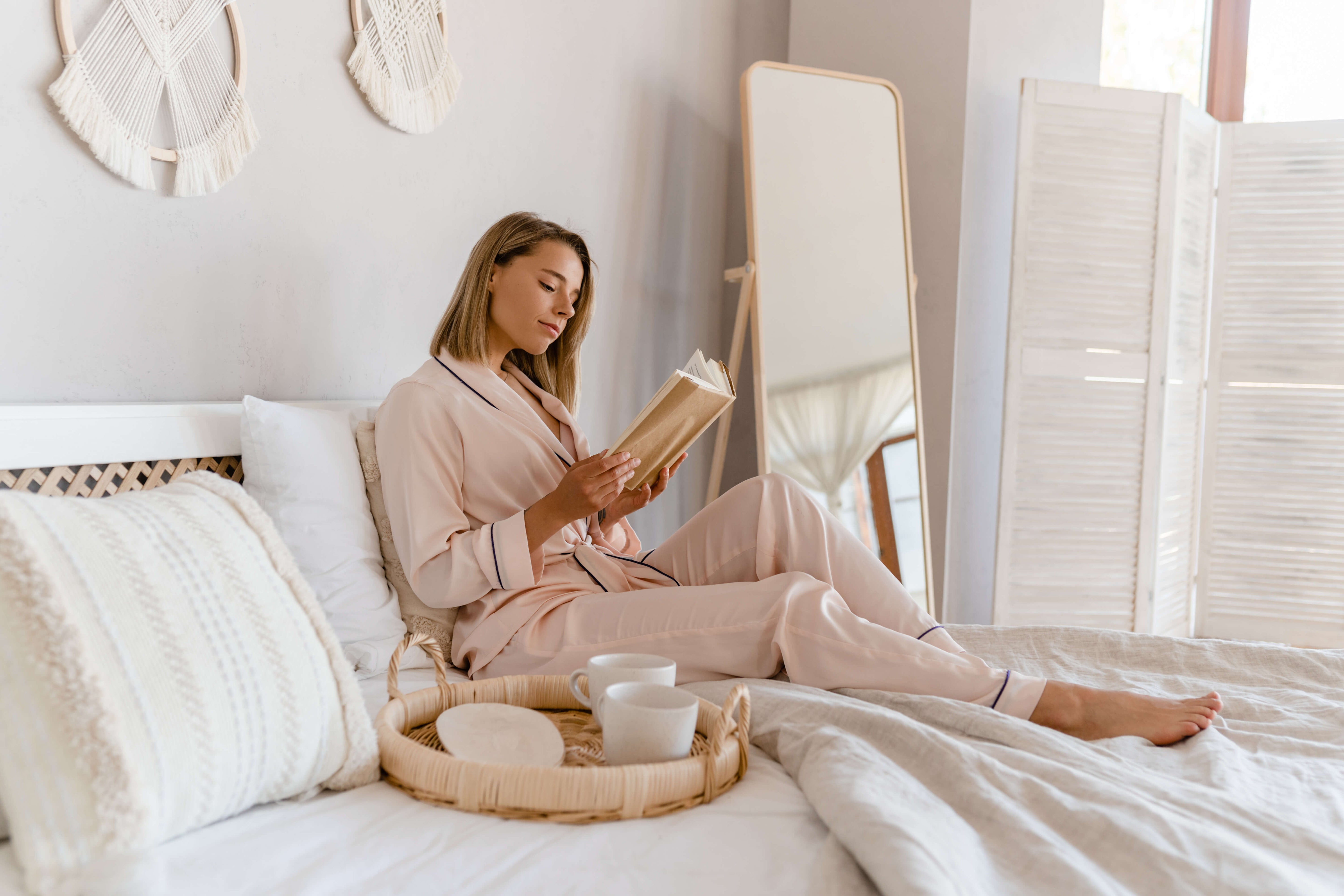 Woman reading a book on a bed in a bright bedroom