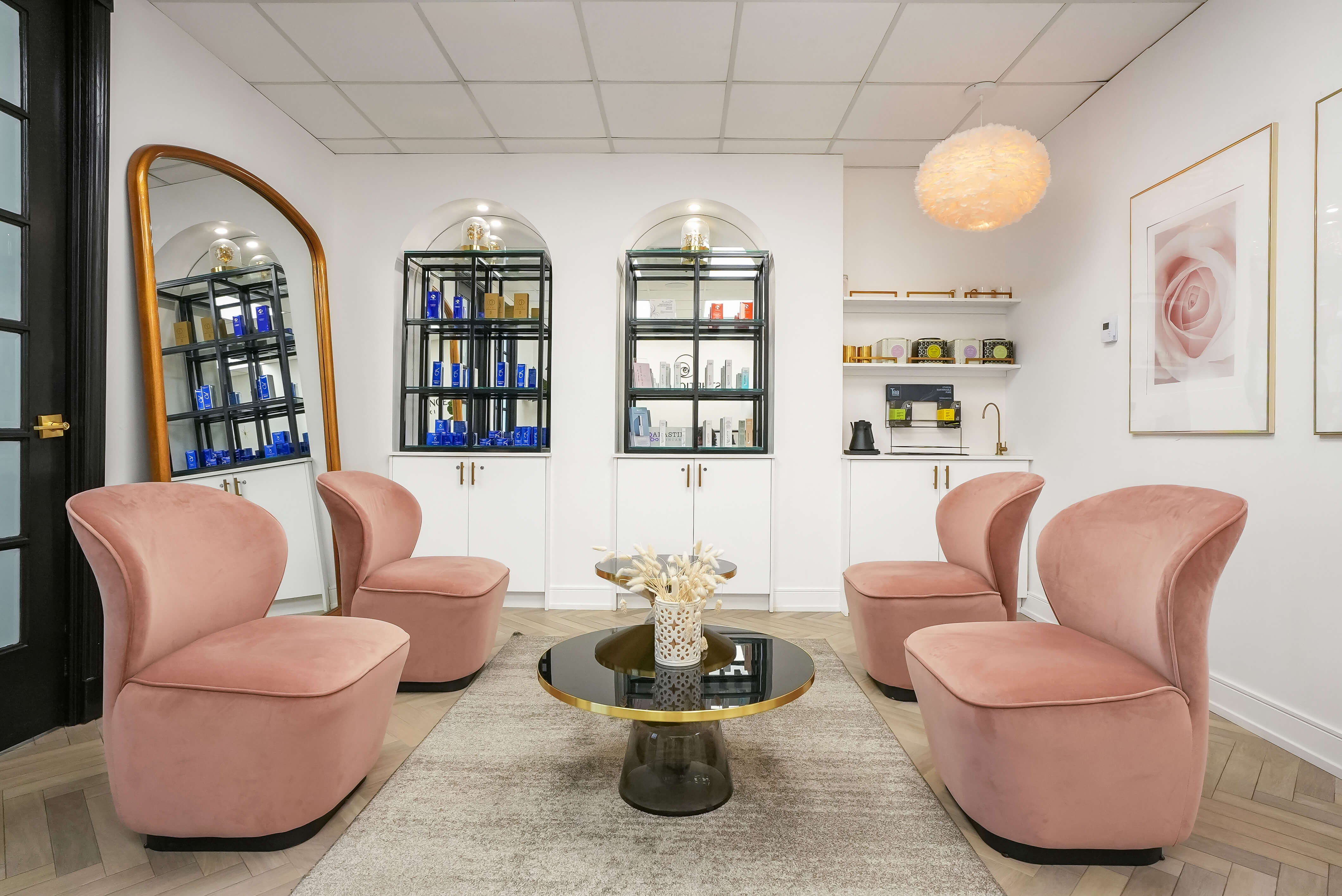 Chic and cozy waiting lounge at Aesthetic Lounge by Dr. Maleki, featuring blush pink chairs, gold accents, and modern shelving with skincare products