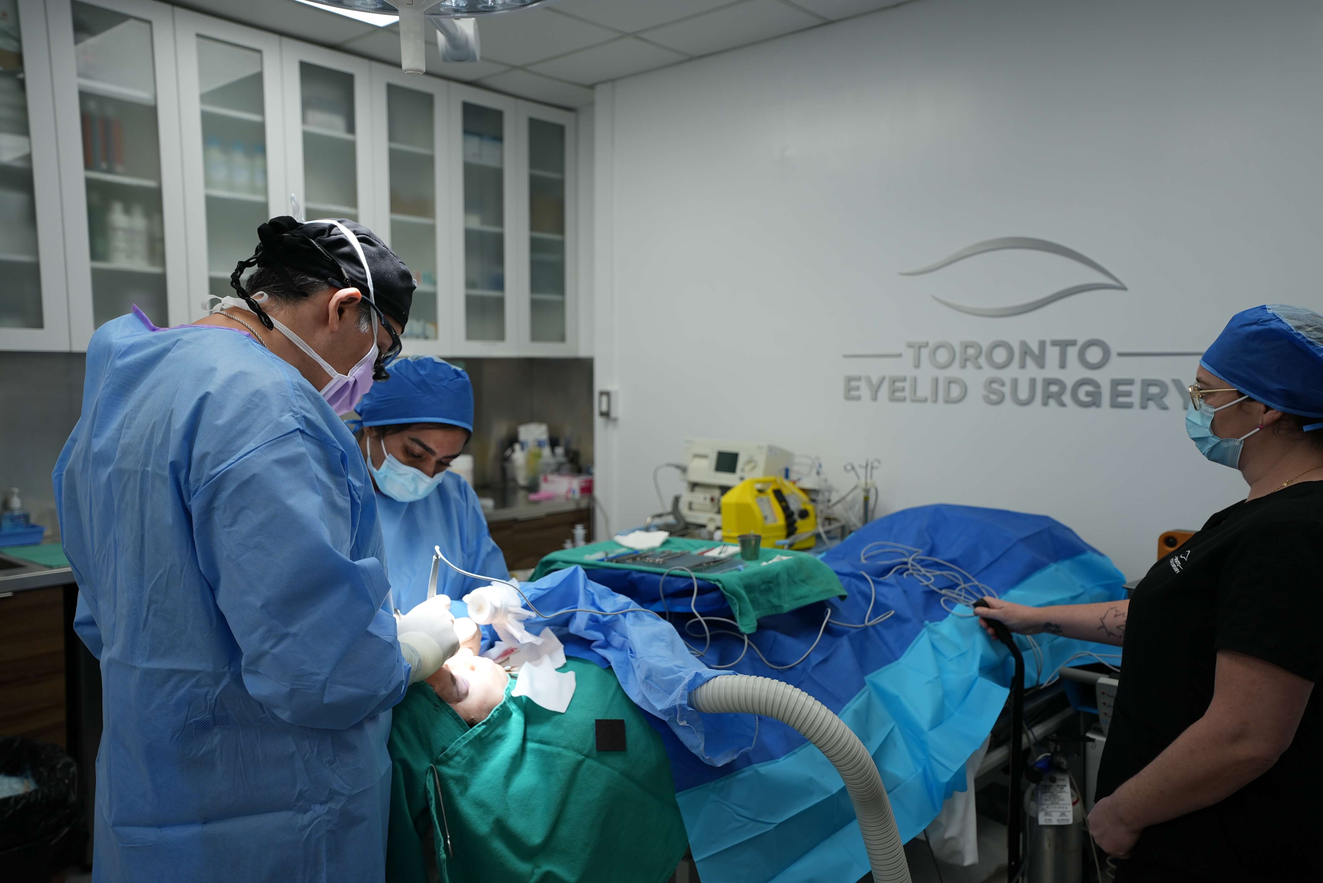 Medical team in an operating room with 'Toronto Eyelid Surgeon' branding on the wall.