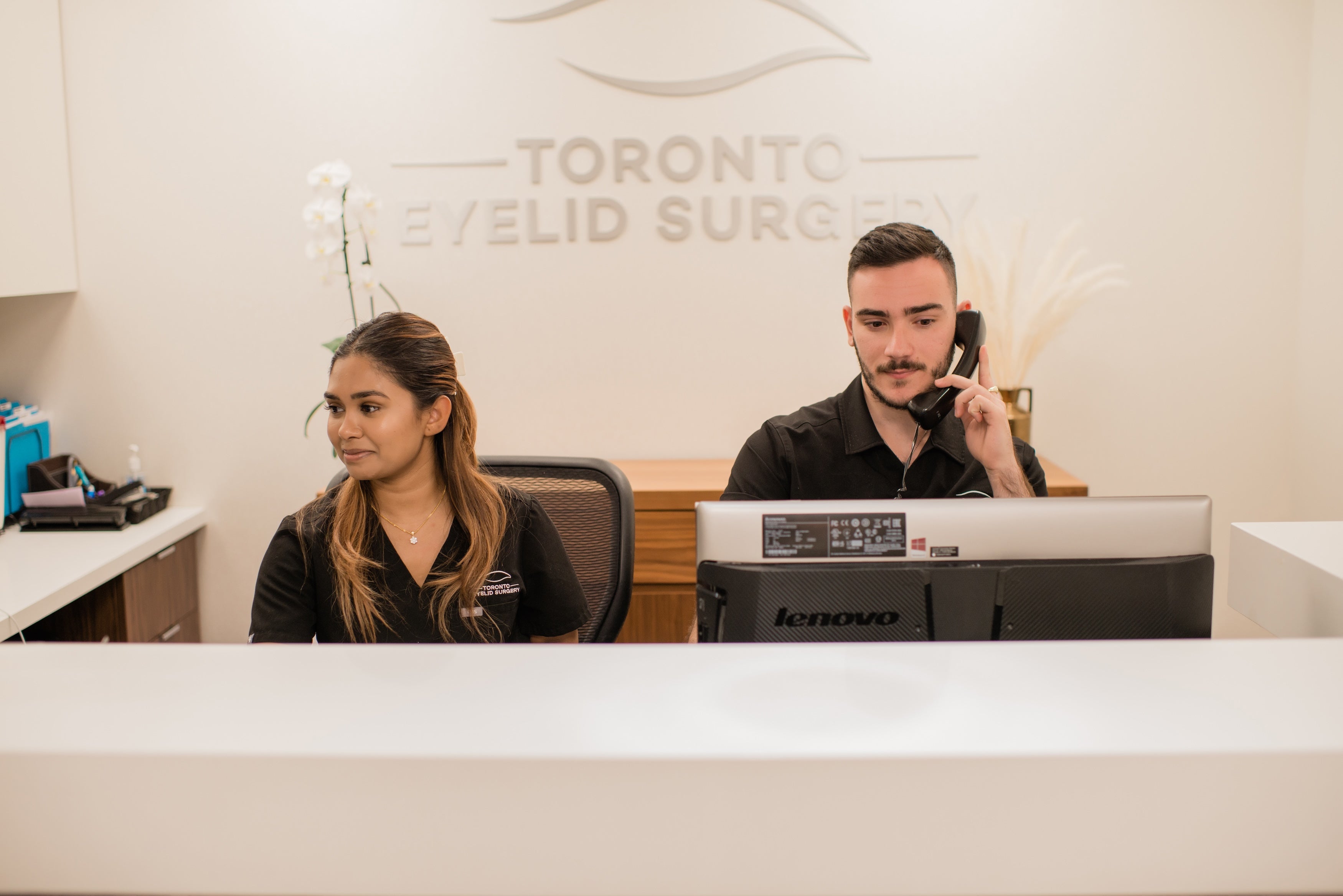 Front desk staff at Toronto Eyelid Surgery clinic assisting patients with appointments and inquiries in a modern reception area