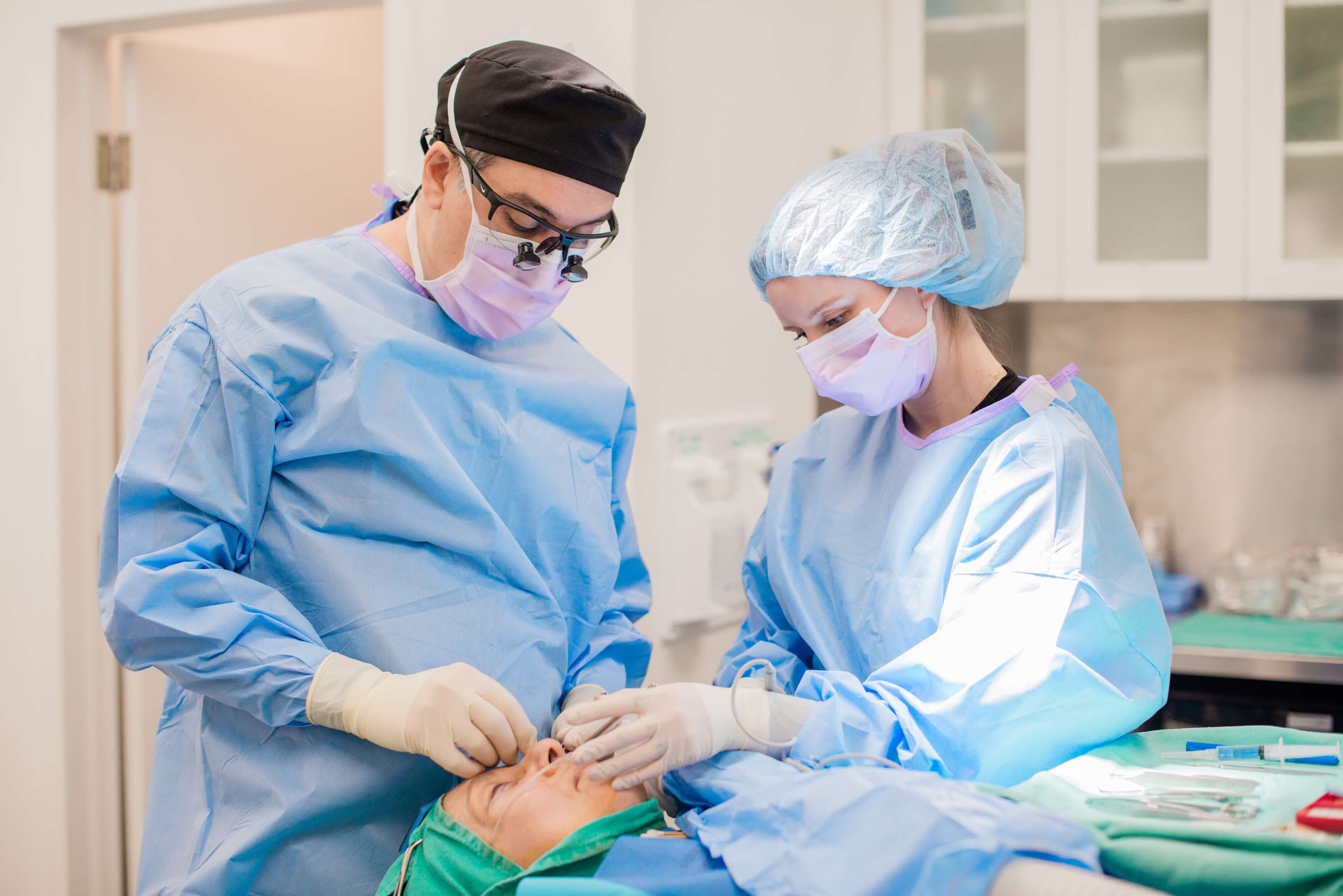 Dr. Babak Maleki performing a facial procedure in a sterile surgical environment with medical team support