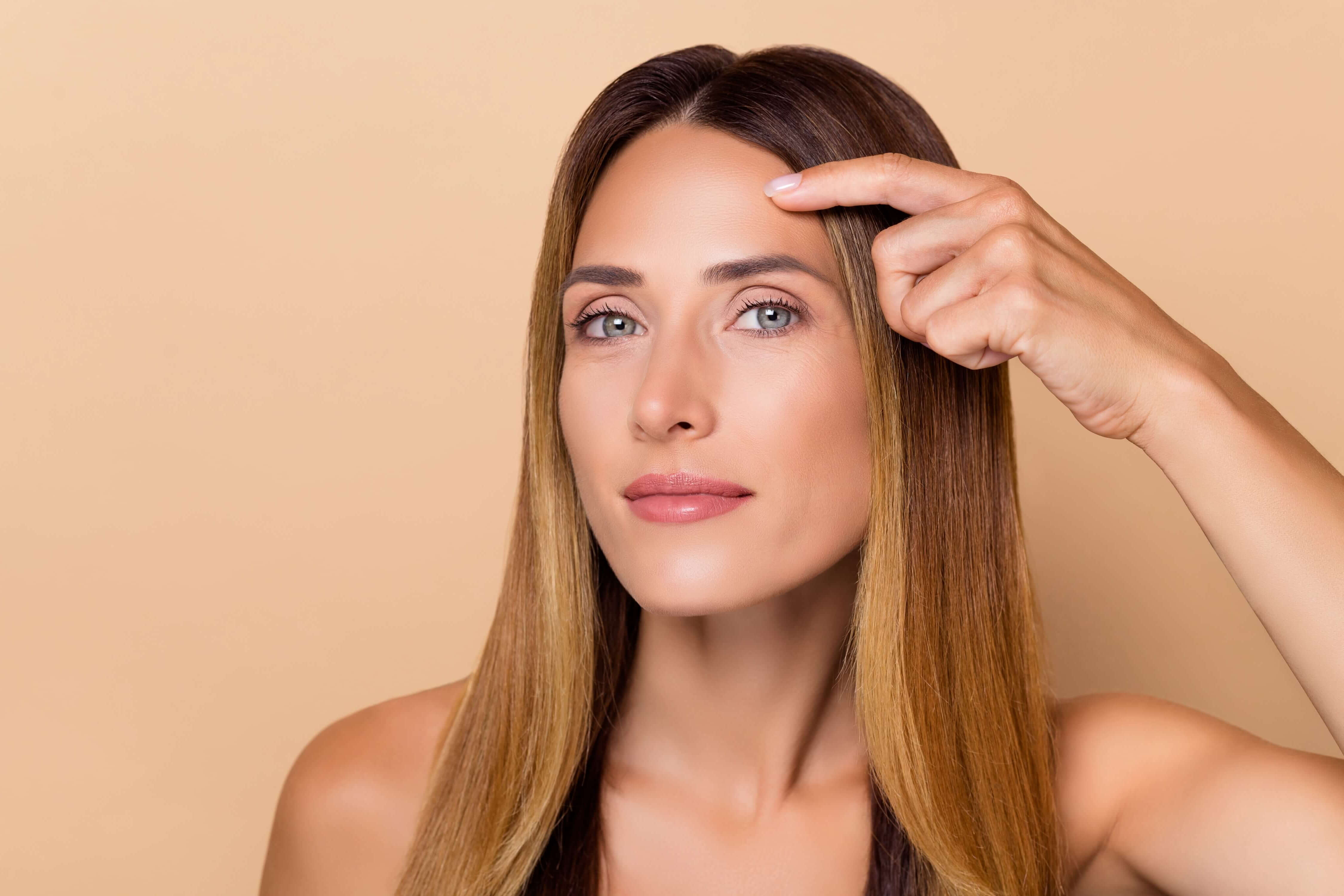 Woman with long brown hair touching her forehead against a beige background