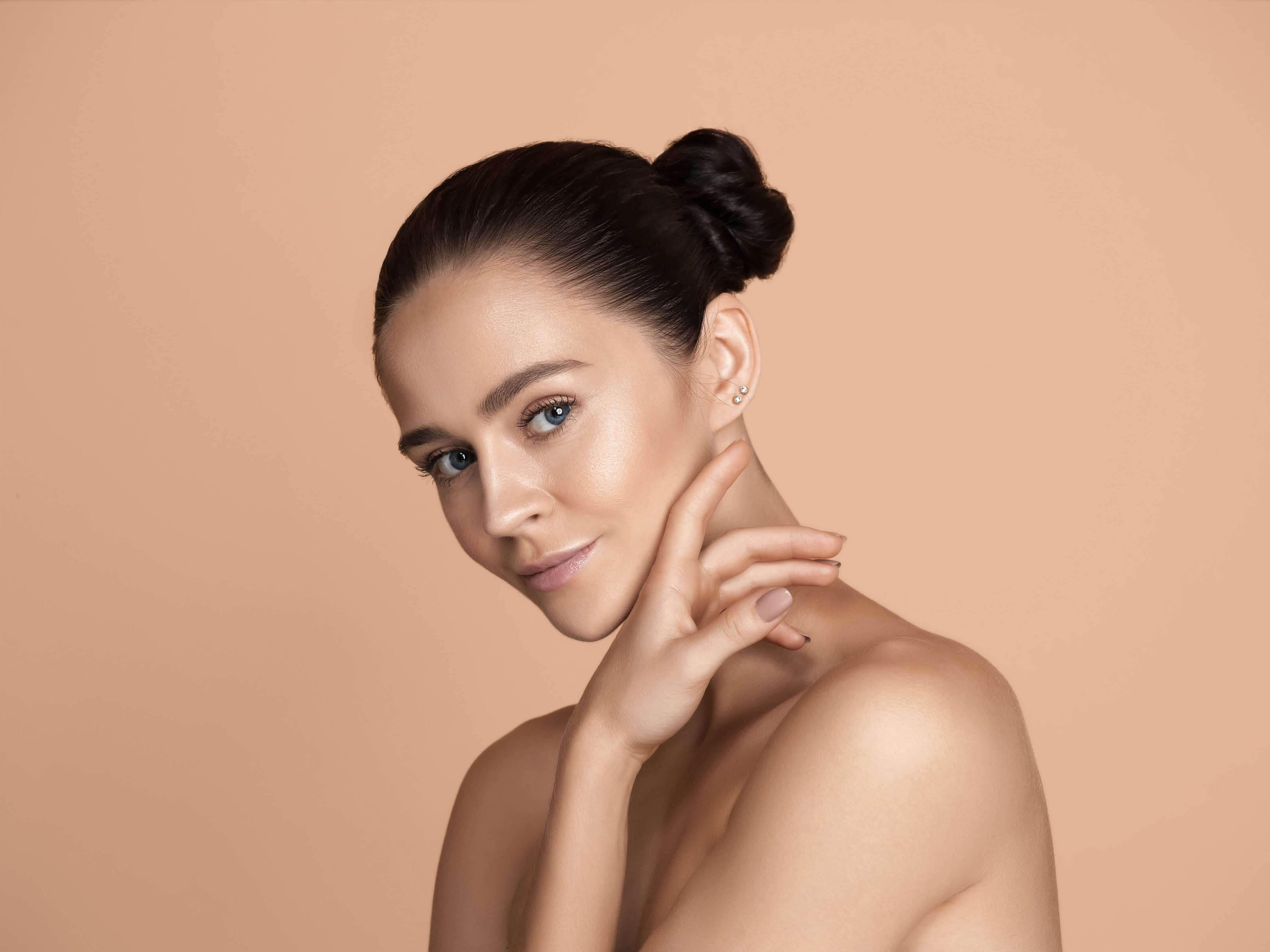 Confident woman with glowing skin posing against a soft nude background, showcasing clear and youthful complexion