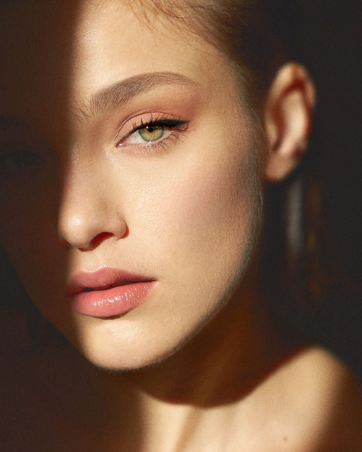 Close-up of a young woman’s glowing face with soft makeup and dramatic lighting, highlighting natural beauty and facial symmetry