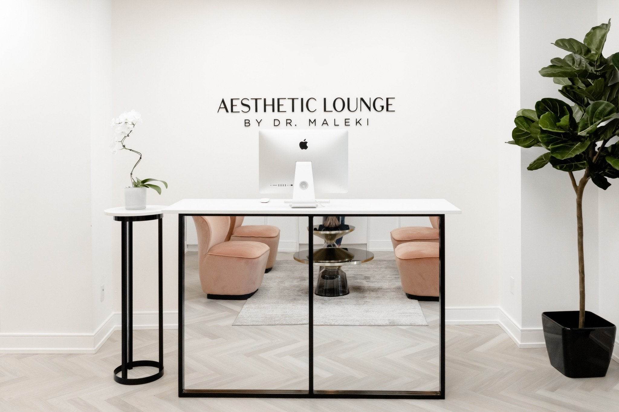 Modern and elegant front desk area of Aesthetic Lounge by Dr. Maleki, featuring blush seating, white marble, and minimalist decor