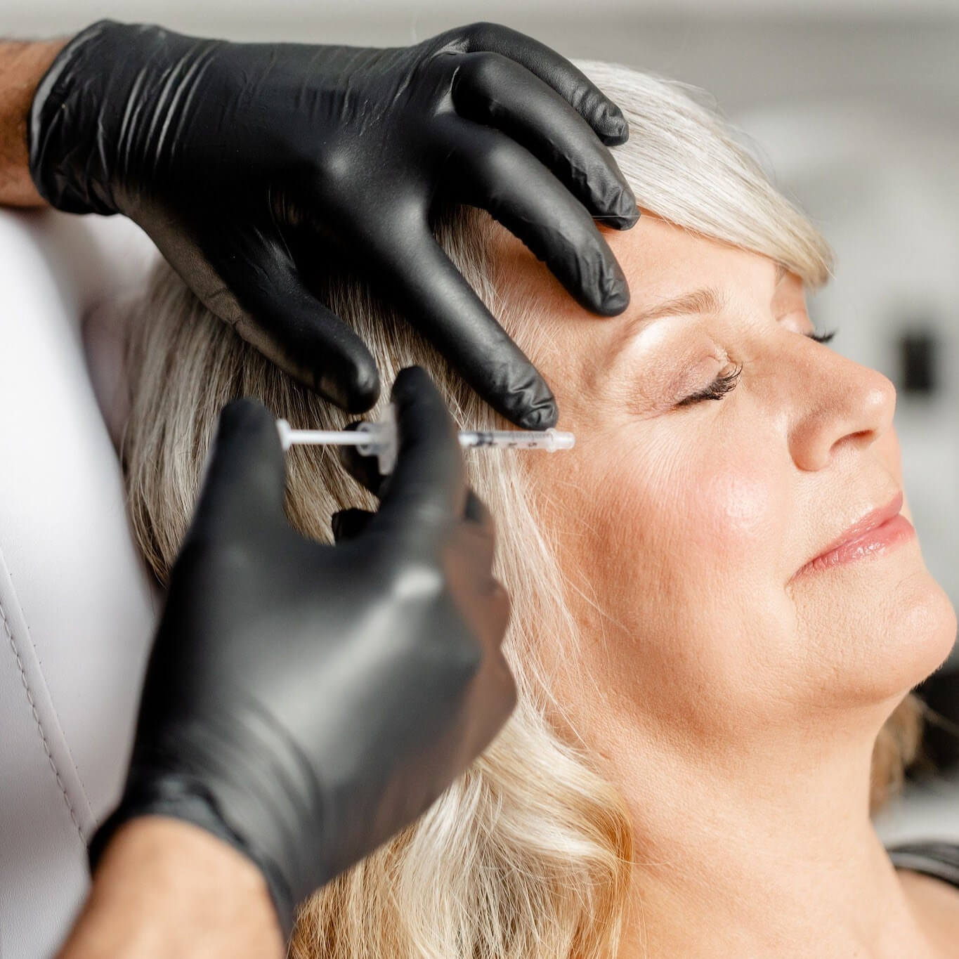 Mature woman receiving aesthetic injection around the eye area by professional in black gloves, showcasing precision and care in anti-aging treatment