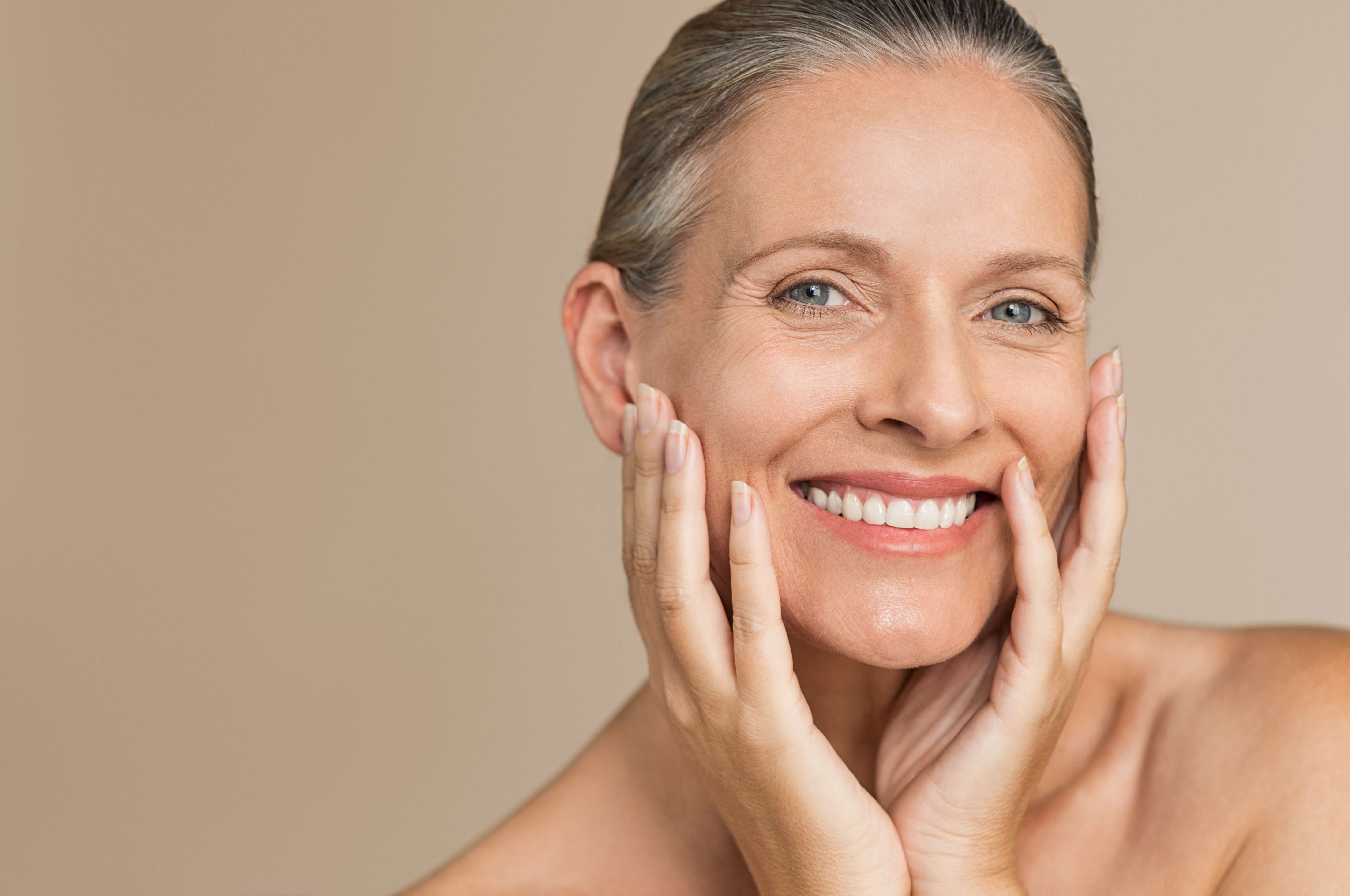 Woman with clear skin touching her face against a beige background
