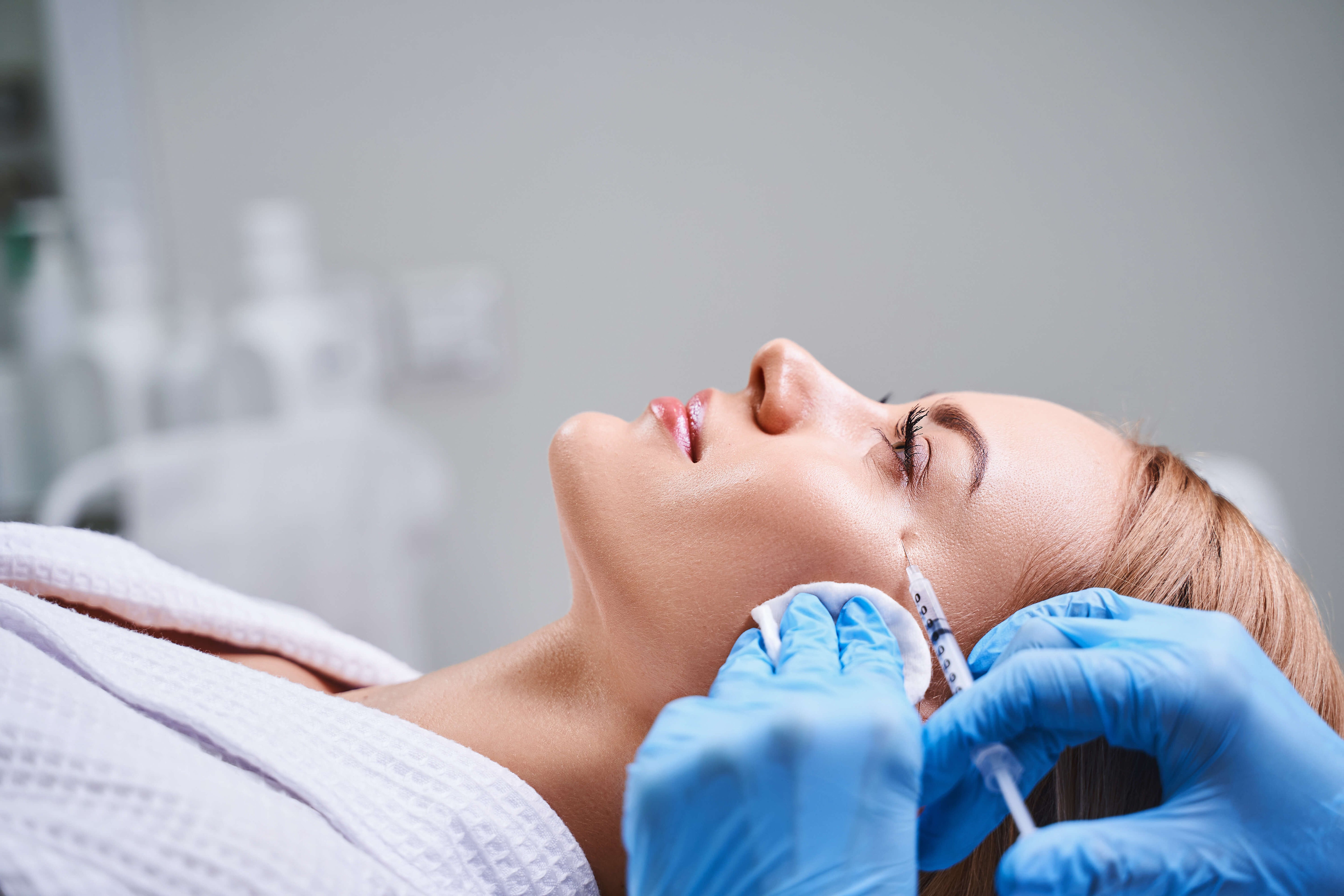 Woman receiving Sculptra injection in the cheek area by medical professional wearing blue gloves