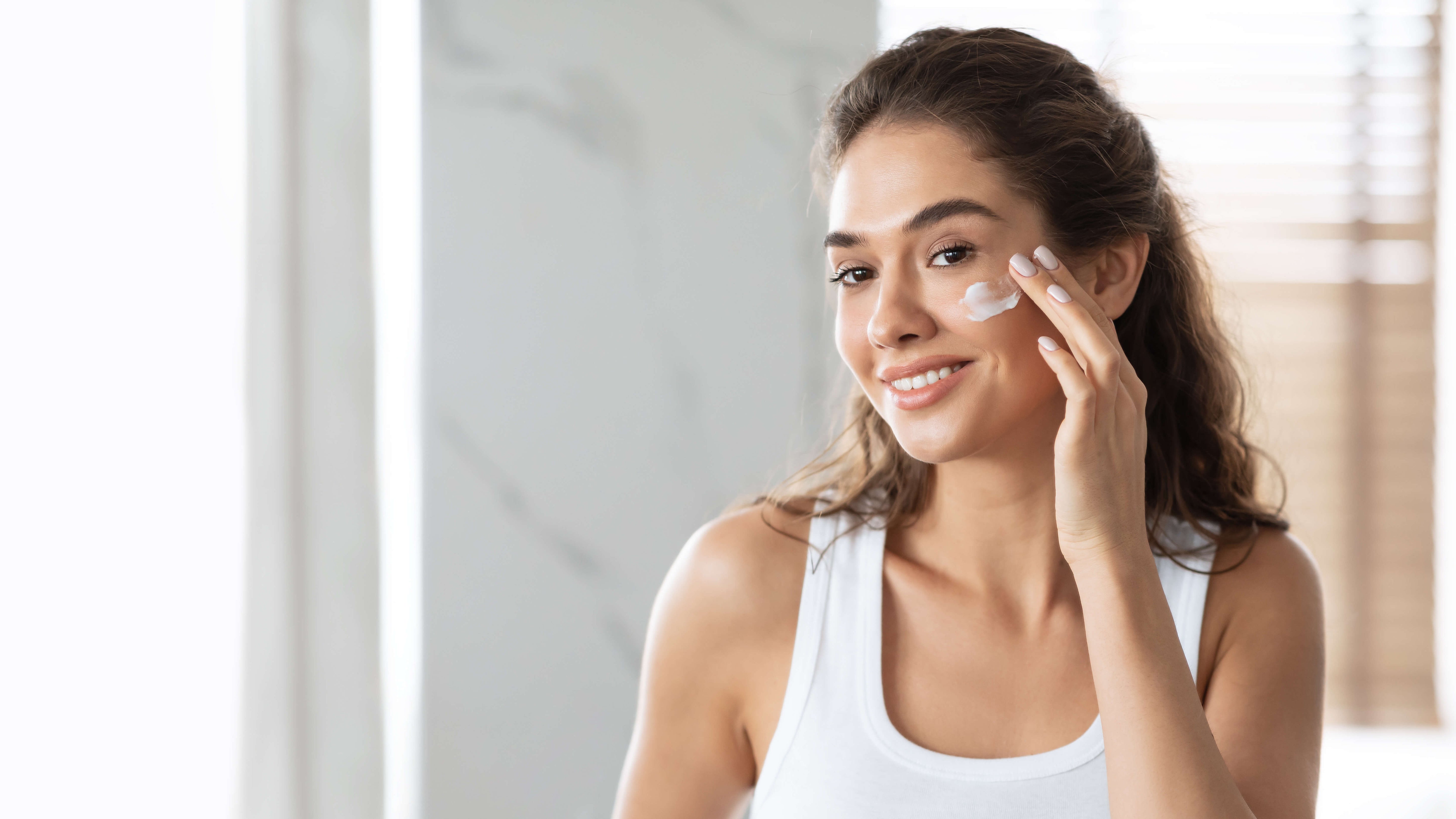 Woman applying cream to her face in a bright room