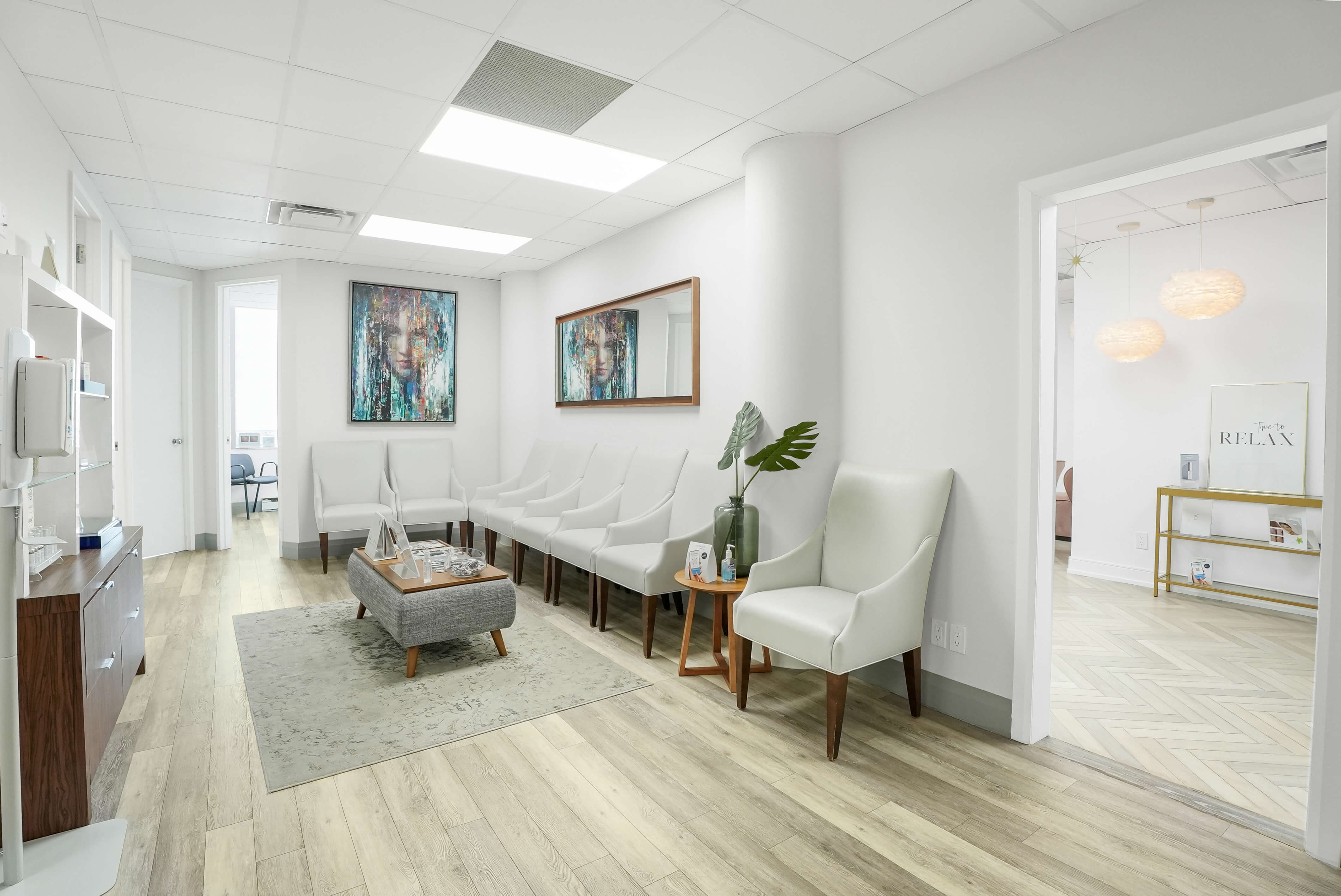 Modern medical clinic waiting area with white chairs, artwork, and natural wood flooring at Dr. Babak Maleki's Toronto practice