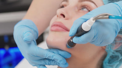 Close-up of a woman receiving a Dermal Infusion Hydrafacial treatment with a professional using a blue-tipped device and wearing blue gloves